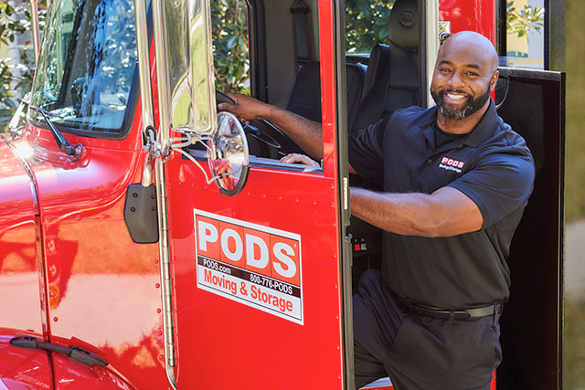 A PODS truck driver getting out of the driver's door of a red PODS truck